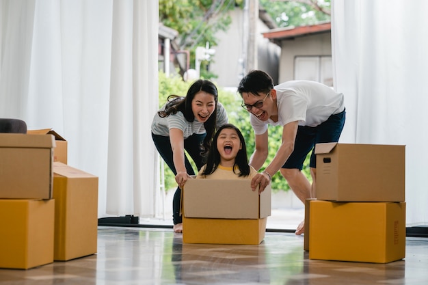 happy-asian-young-family-having-fun-laughing-moving-into-new-home-japanese-parents-mother-father-smiling-helping-excited-little-girl-riding-sitting-cardboard-box-new-property-relocation_7861-2290